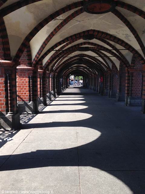 Red brick arcade with vaulted ceilings, arch shadows cast on the pavement