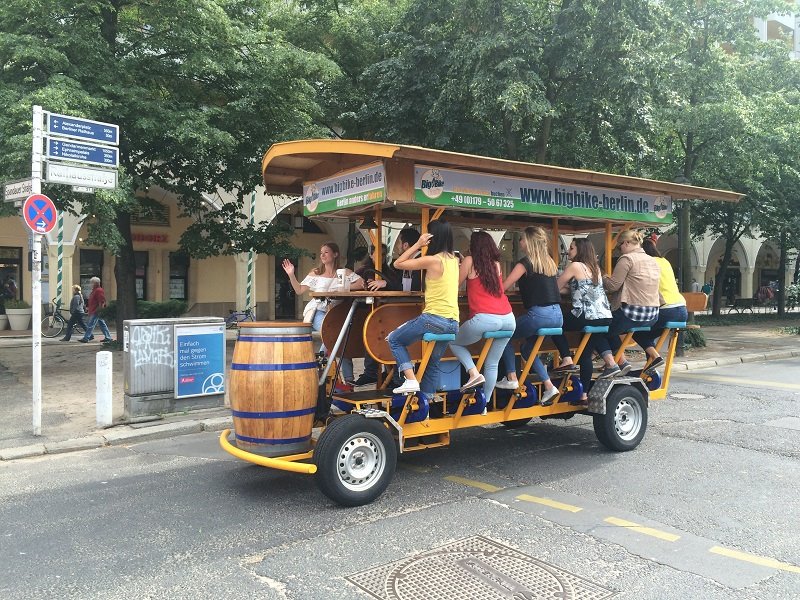 Gruppo di turisti pedala su una birreria mobile gialla con botte di legno per Berlino