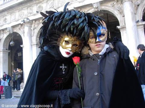 Costumed masks in St Mark's Square, Venice: golden faces, black feathers, red rose