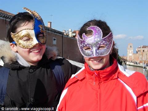 Two children wearing carnival masks in Venice, canal and bell tower behind