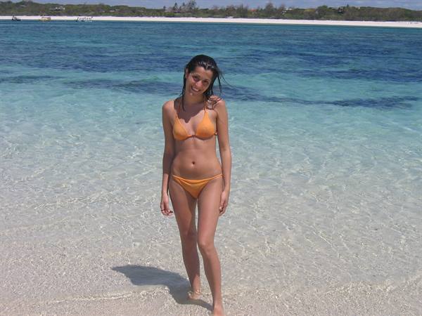 Woman in orange bikini walks on white sand, shallow turquoise sea