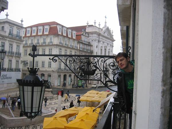 Young man on a balcony with wrought-iron lamp and yellow umbrellas, Lisbon