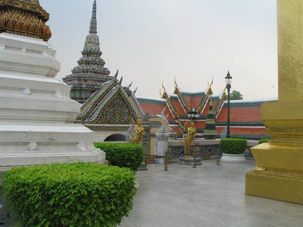 Wat Arun in Bangkok: golden statues, white stupa and colorful roofs among shrubs