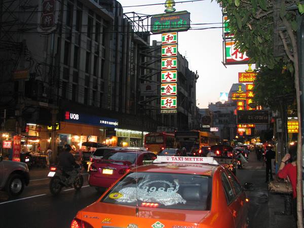 Orange taxi in Bangkok Chinatown traffic under glowing neon signs