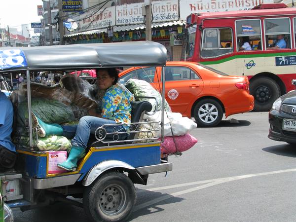 Woman in green boots on tuk-tuk loaded with vegetables, city traffic