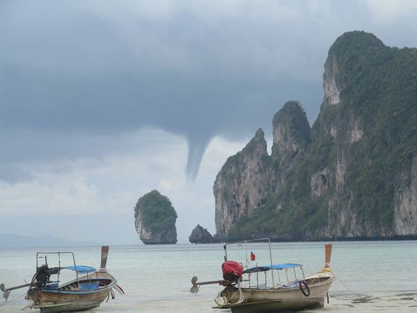 Longtail boats on Phi Phi beach with a waterspout between limestone cliffs