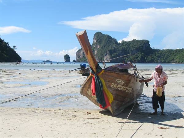 Wooden longtail boat stranded on sand, man with bucket, Phi Phi beach
