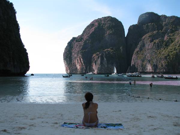 Woman sitting on the sand at Maya Bay, limestone cliffs and boats