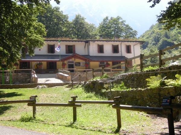 Mountain refuge of stone and wood, with a flag and wooden fence among trees