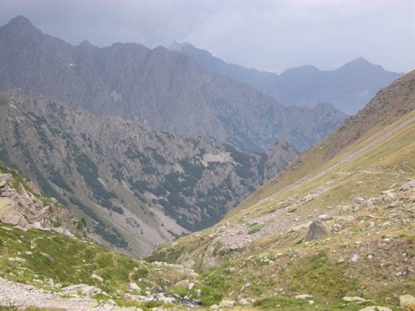 Grassy rocky valley between bare mountains under grey cloudy sky