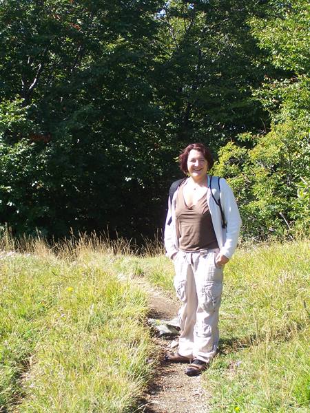 Smiling woman with backpack on grassy trail among sunlit trees