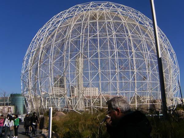 Visitors crouching in front of Montreal's geodesic Biosphere under blue sky