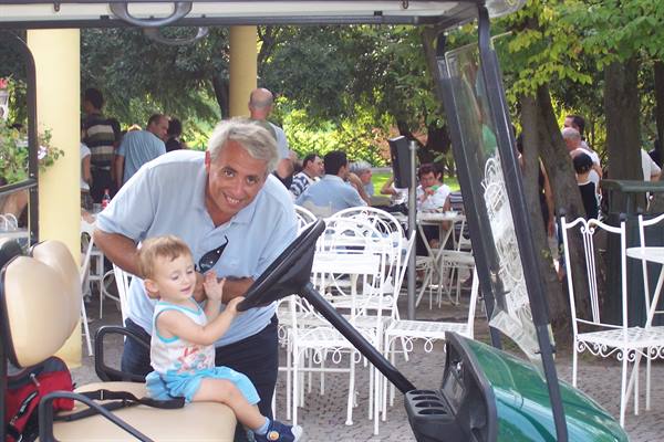 Man smiles as a toddler plays with a golf cart steering wheel