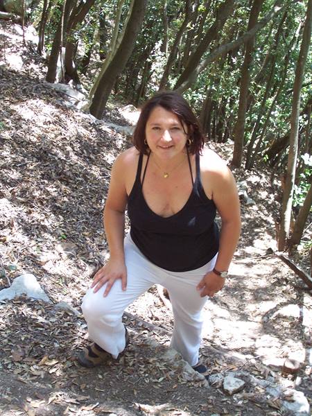 Woman in black top and white pants climbing a rocky woodland trail