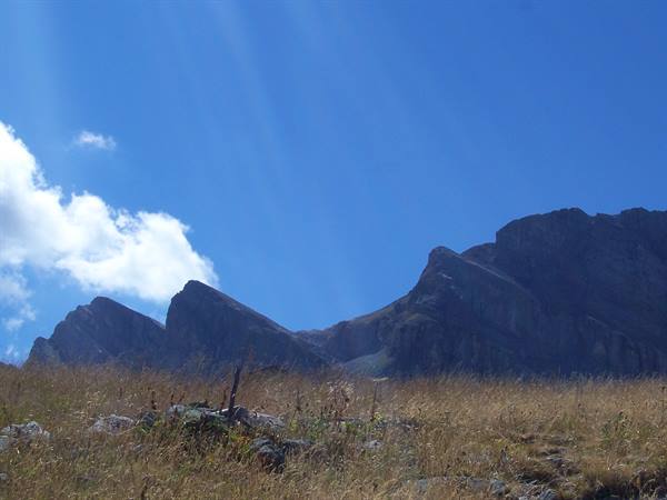 Dark rocky peaks above a dry golden meadow under blue sky with clouds