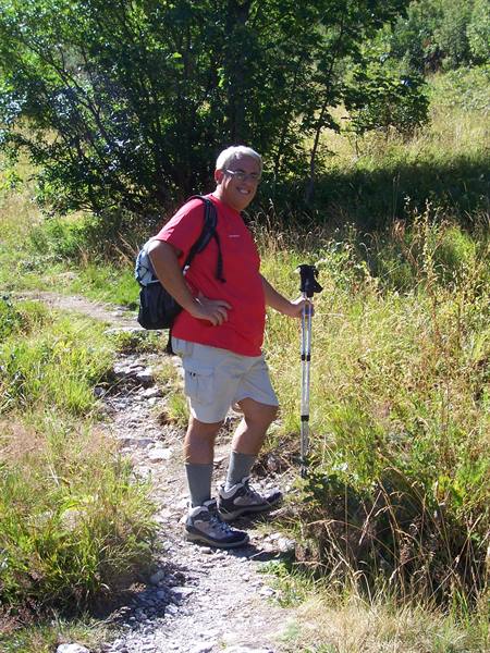 Man in red shirt with backpack and trekking pole on grassy trail