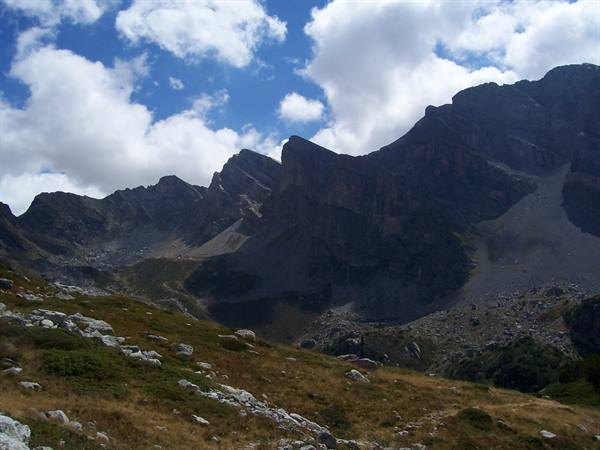 Rocky ridges above stony alpine pastures, white clouds in blue sky