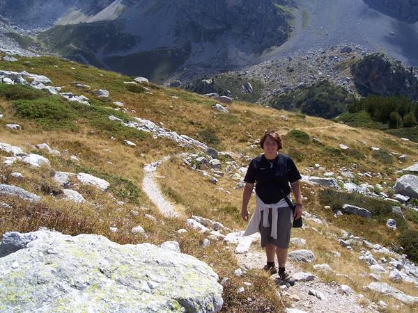 Woman in black shirt walks on rocky trail amid dry grass and mountains