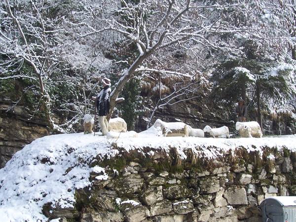 Shepherd statue with snow-covered sheep atop a stone wall