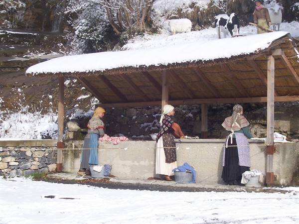 Women in traditional dress washing at a snow-covered stone washhouse