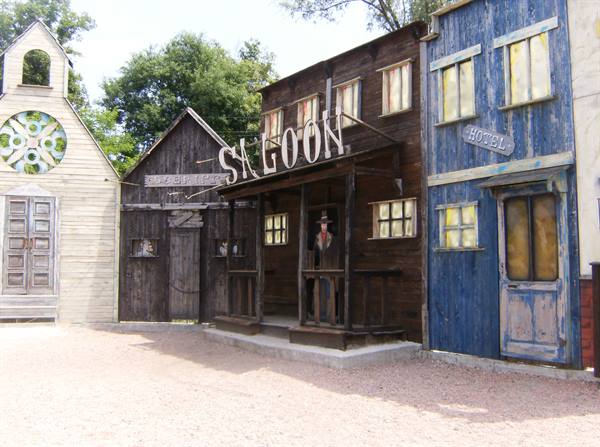 Wooden western town with saloon and hotel, cowboy standing under the porch