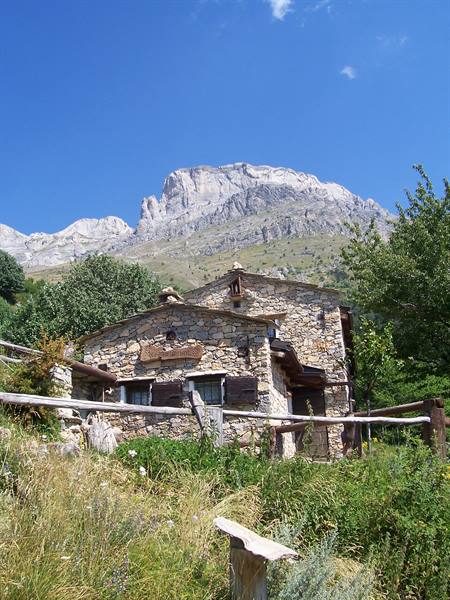 Stone farmhouse with wooden fence beneath a rocky peak