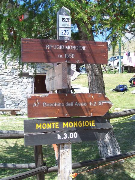 Wooden trail signs to Rifugio Mongioie and Monte Mongioie among larches and stone houses
