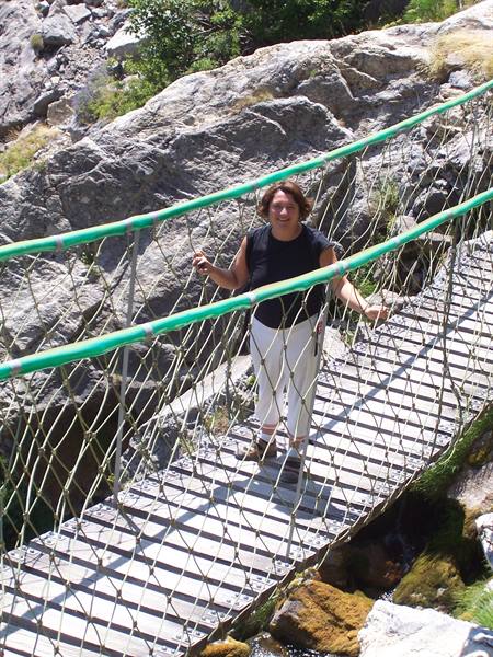 Woman smiling on suspended metal footbridge between granite rocks and greenery