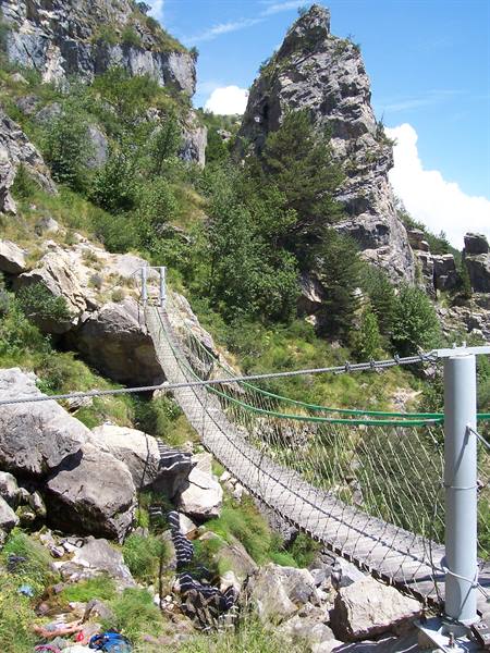 Rope suspension bridge with steel cables among rocky cliffs and pines