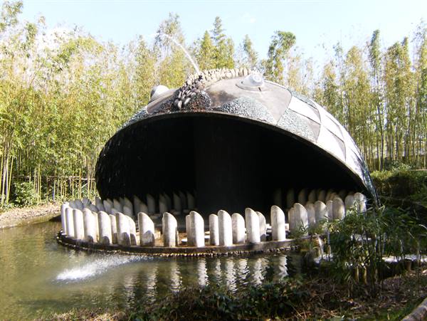 Fountain shaped like a head with white teeth in a pond among bamboo, Tarot Garden