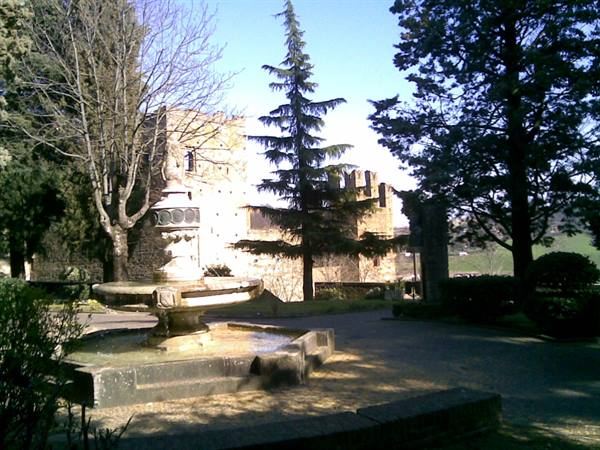 Stone fountain in front of castle walls, among trees under blue sky