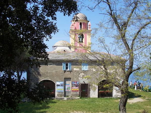 Church with pink bell tower among trees, overlooking the sea