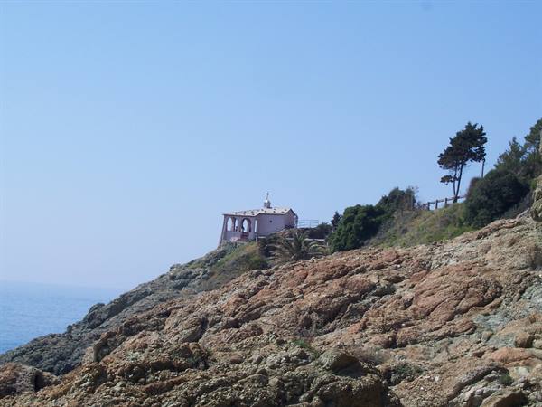 Small white chapel with dome atop red cliffs above the sea