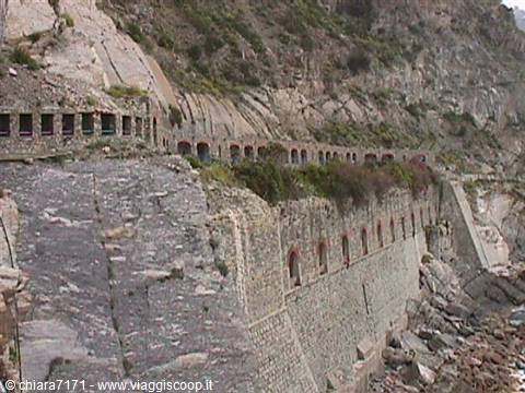 Arched road carved into the cliff above dry-stone sea walls