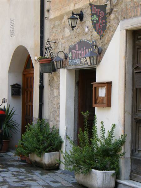 Wooden sign of Il Torchietto restaurant on stone wall, lanterns and shrubs