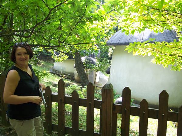 Smiling woman beside wooden fence among mushroom-shaped houses in green woods