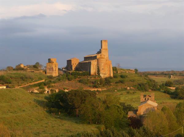 Ancient Romanesque stone basilica on the hill, green hills under cloudy sky