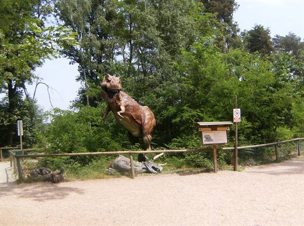 Dinosaur statue among trees, wooden fence and information sign