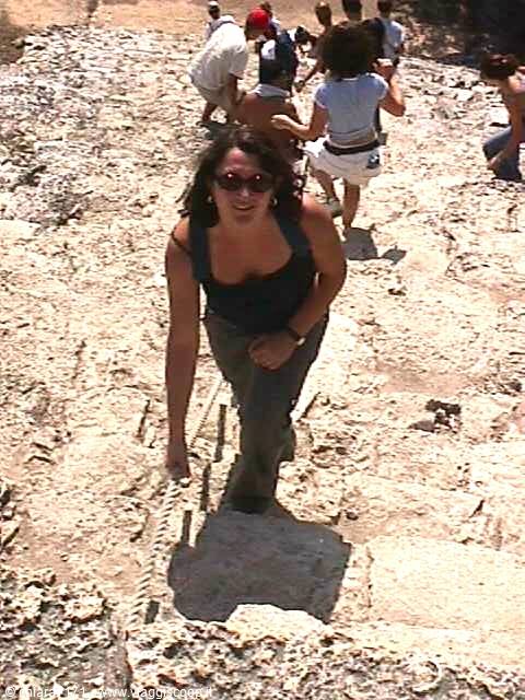 Woman in sunglasses climbing ancient stone steps, tourists behind her