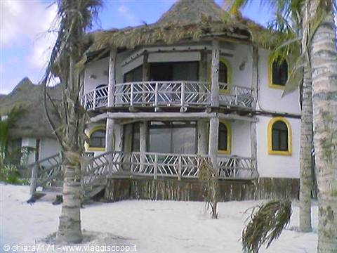 Two-story thatched bungalow with wooden balconies among palm trees on white sand
