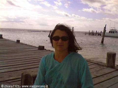 Woman in sunglasses on a wooden pier, boat and sea behind