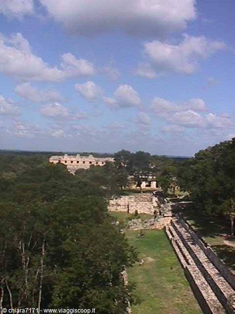 Ancient Maya stone ruins among green trees, blue sky with clouds