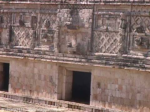 Maya stone facade with carved masks and dark doorways at Uxmal
