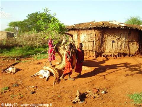 Maasai children in red clothes beside mud huts on red soil