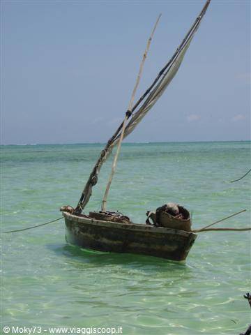 Old wooden sailboat anchored in clear turquoise shallow water