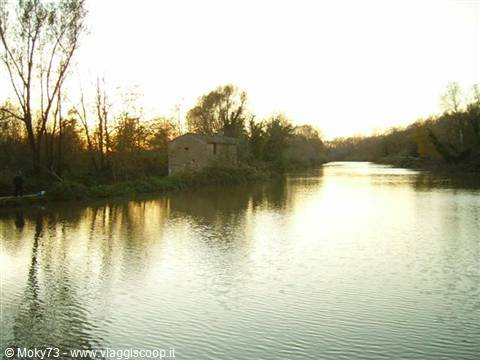 Calm river with small brick house among bare trees, low light