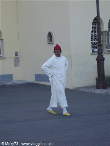 Man in white djellaba and red fez walks along the street