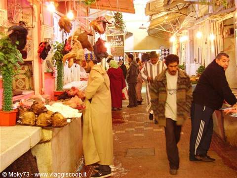 Souk in the medina: butcher with hanging meat and passersby among stalls, Marrakech