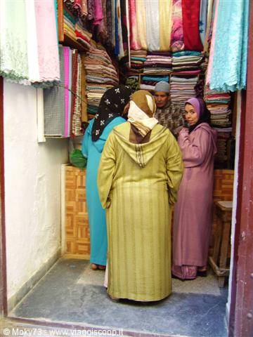 Women in djellabas shopping among colorful fabrics at an imperial city souk