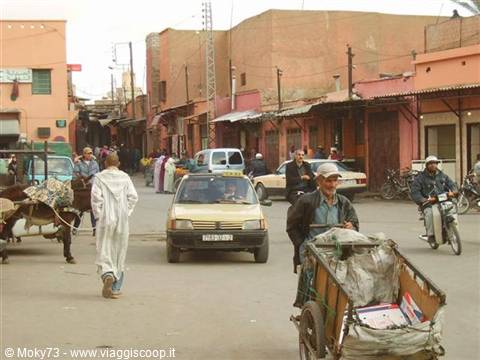 Man with cart on a Marrakech street, ochre houses, taxi and passersby